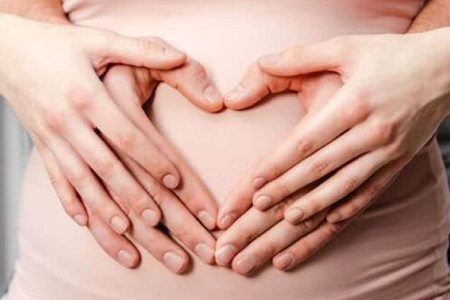 Expectant mother with partner holding hands around the baby bump in shape of a heart