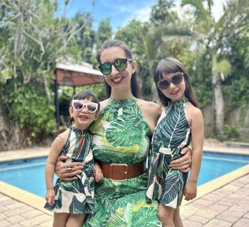 A woman and two children in sunglasses and green dresses smiling outdoors.