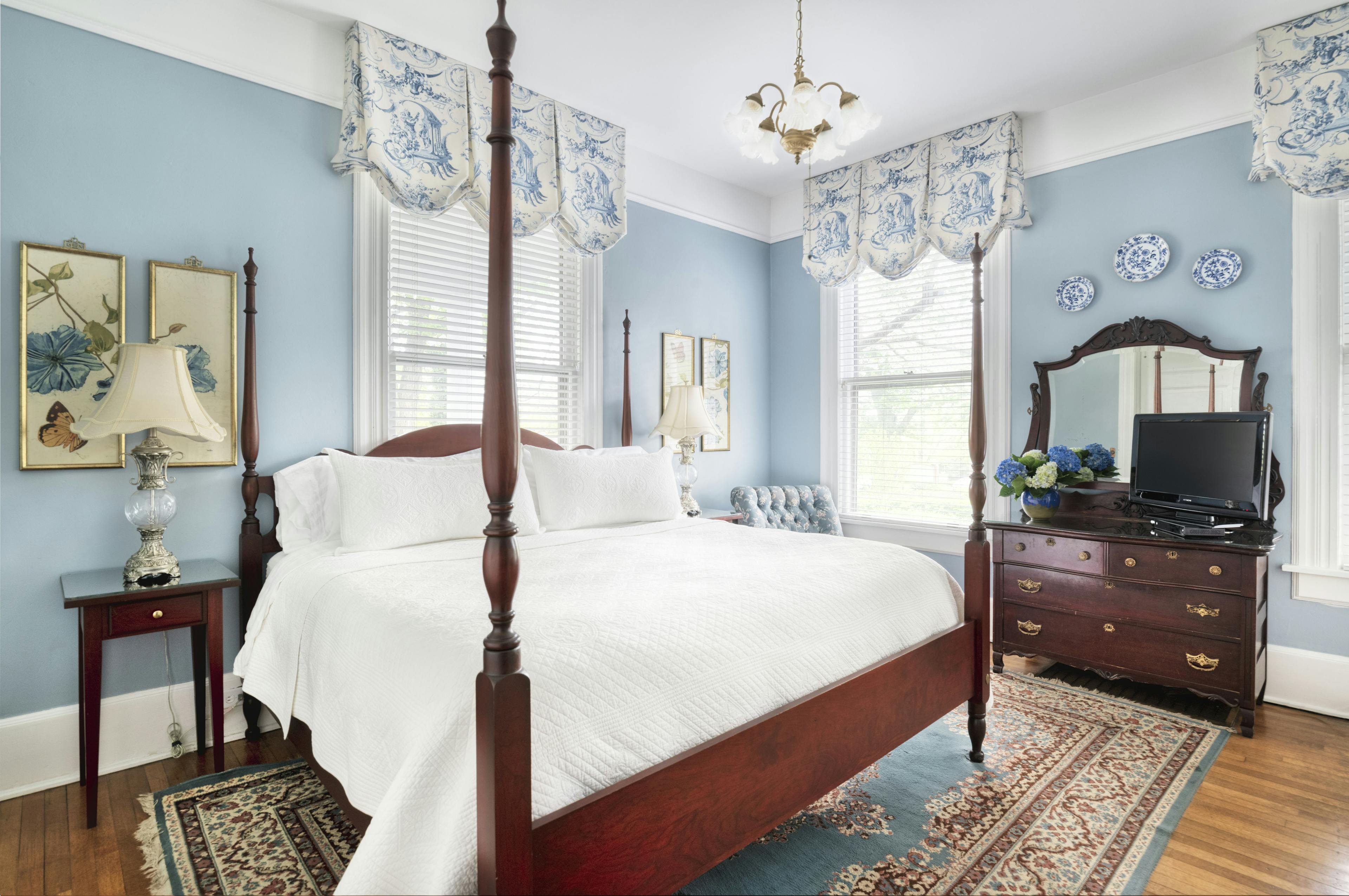 Victorian four post bed with white sheets. The room has hardwood floors and the walls are painted baby blue.
